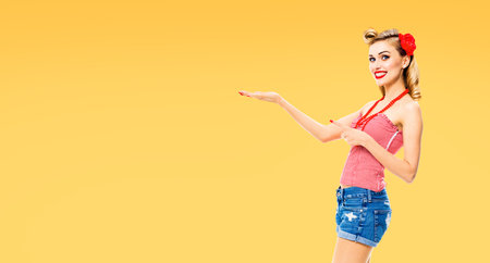 Happy smiling woman pointing at something. Excited girl in pin up, showing, holding some product or...