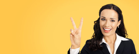 Businesswoman in black confident suit showing two fingers or victory gesture, over orange yellow...