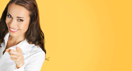 What about You? Image of happy smiling woman in white confident clothing pointing finger at viewer. Business concept. Orange yellow colour background. Brunette businesswoman.の写真素材