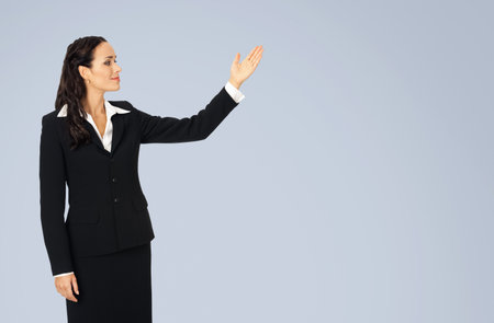 Photo image of happy smiling woman in black confident suit, showing at copy space. Business concept. Isolated over grey background. Brunette businesswoman.の写真素材