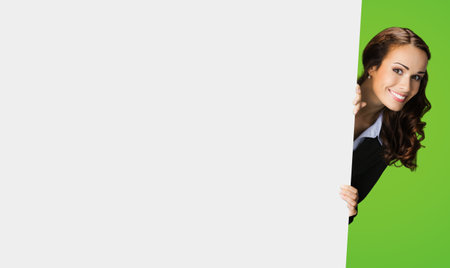Photo of happy smiling woman in black confident suit, peek out showing mock up white banner signboard with copy space area for sign text. Business and ad concept. Green color background.の写真素材