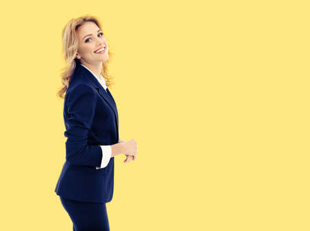 Portrait of happy smiling young businesswoman in dark blue confident suit, isolated on yellow color background. Business studio concept. Copy space blank area for text.の写真素材