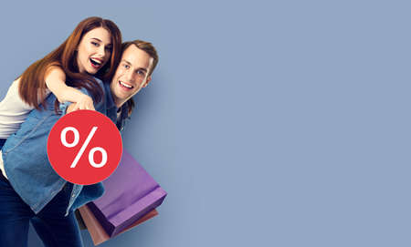 Holiday sales actions, rebates, discounts, store retail, trade, consumer concept image - happy excited young couple with shopping bags, in piggyback pose. % sign text.の写真素材