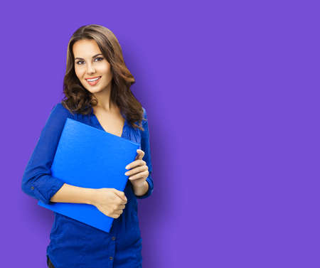 Portrait of happy smiling young brunette woman in blue confident wear with folder, isolated on violet purple color background. Business studio concept. Copy space blank area for text.の写真素材
