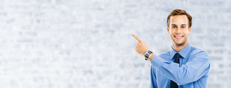 Confident businessman pointing showing advertising something, over white brick loft wall background. Copy space area for some text. Success in business, job or education concept.の写真素材