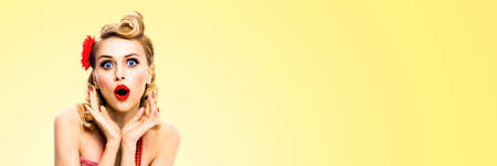 Unbelievable news! Excited surprised, very happy blondy hair woman. Pin up syle girl with open mouth and raised hands. Retro and vintage studio concept. Light yellow color background.の写真素材