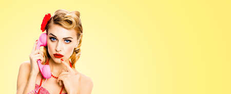 Portrait studio image - pensive, puzzled or thinking woman with phone tube. Unhappy pin up girl. Retro and vintage concept. Light yellow color background with copy space. Wide banner composition.の写真素材