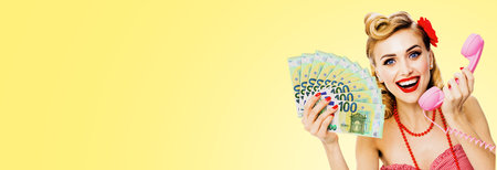 Photo of happy excited woman holding money euro cash banknotes, talking on phone, dressed in pin up style. Blond girl in retro fashion and vintage concept. Light yellow background.の写真素材