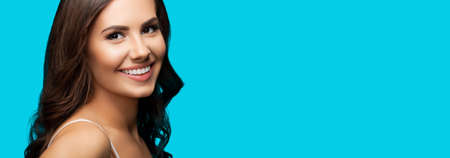 Portrait of smiling beautiful woman in white casual wear looking at camera, over aqua blue background. Brunette girl at studio concept. Wide composition.の写真素材