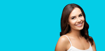 Portrait of cheerful smiling woman in white casual clothing, isolated on aqua blue background. Brunette girl posing at studio. Wide composition with copy space free area for text.の写真素材