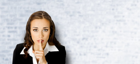 Portrait of young serious business woman keeping finger on her lips and asking to keep quiet, on...