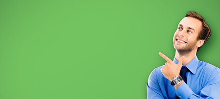 Looking up, smiling businessman pointing showing something, over green color background. Business, job and education coach concept. Confident man pointing at copy space.の写真素材