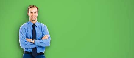 Portrait of happy smiling businessman, standing in crossed arm pose, over green color background. Confident business man. Copy space area for text.の写真素材