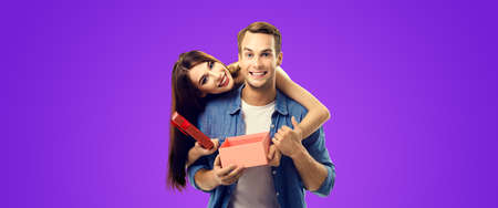 Love, relationship, dating, flirting, lovers, romantic concept - happy couple opening gift box, looking at camera. Purple violet color background. Valentines Day holiday. Copy space.の写真素材