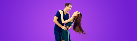 Love, relationship, dating, flirting, lovers, romantic concept - portrait of hugging or dancing couple, looking at each other. Purple violet color background.の写真素材