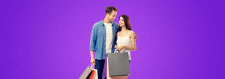 Love, holiday sales, shop, retail, consumer concept - happy couple with shopping bags, looking at each other. Purple violet color background. Valentines Day holiday. Copy space.の写真素材