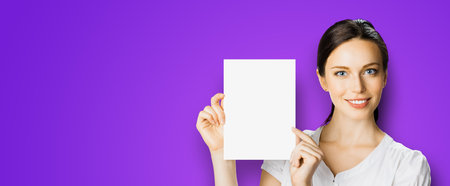 Studio portrait image of smiling woman in white cloth, hold showing demonstrate mock up paper signboard. Business and advertising concept. Copyspace empty free area for text. Violet purple background.の写真素材