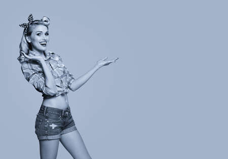 Young happy smiling woman, dressed in pin up style, showing something or copyspace area for text or slogan. Blond girl posing in retro fashion and vintage concept. Black and white.の写真素材