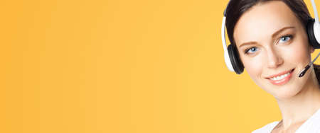 Call center help line service. Face portrait image of customer support phone sales operator in headset, on orange yellow. Brunette business woman. Adviser.の写真素材