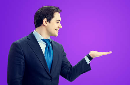 Smiling senior businessman holding, giving, showing something or copy space area for sign or slogan text, profile view side. Marketing and advertising concept. Violet purple background.の写真素材