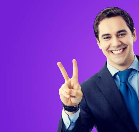 Portrait of confident businessman showing two fingers or victory hand sign gesture, isolated over violet purple background. Middle aged happy smiling business man at studio concept.の写真素材