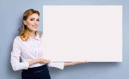 Happy amazed business woman in white confident clothing showing mockup banner signboard. Success in business and advertising concept. Copy space place for some text or imaginary.の写真素材