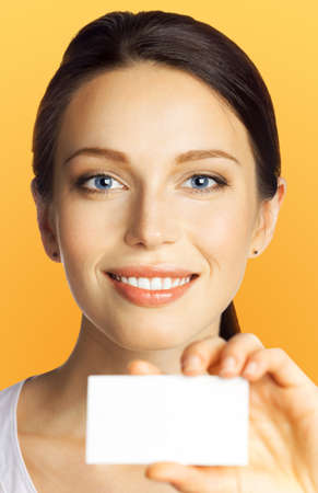 Closeup portrait of smiling businesswoman showing mockup empty businesscard or plastic credit card, with copy space, over orange yellow color background. Brunette business woman at studio image.の写真素材