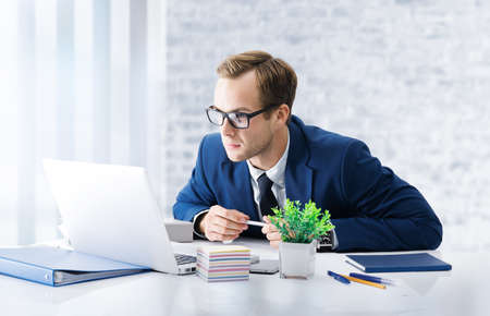 Serious businessman in glasses and blue suit working with laptop computer at office workplace. Condident man in business, job and education concept.の写真素材