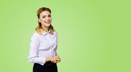 Happy smiling attractive businesswoman, with copy space area for some slogan or text. Confident blond woman in white shirt standing over green colour background. Business concept.の写真素材