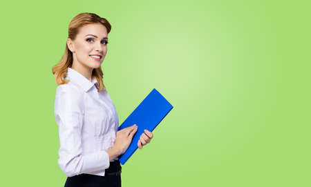 Happy smiling attractive businesswoman, with copy space area for some slogan or text. Confident blond woman in white shirt with blue folder. Green colour background. Business concept.の写真素材