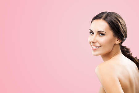 Portrait image of beautiful young happy smiling brunette woman, with naked shoulders, isolated over rose pink background. Copy space area.の写真素材