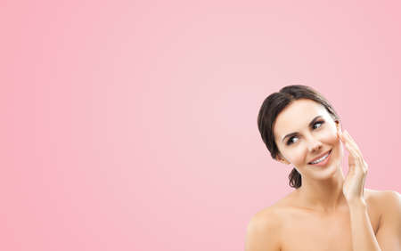Portrait of beautiful dark haired woman cleaning face skin by cotton pad, isolated over rose pink background. Amazed smiling brunette girl at studio. Beauty model picture. Copy space empty text area.の写真素材