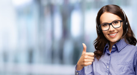 Contact Call Center Service. Customer support, sales agent. Caller or answering phone operator or businesswoman in headset. Business woman in glasses showing thumb up. Blurred office background.の写真素材