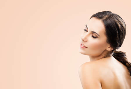 Portrait image of beautiful young woman with closed eyes and naked shoulders, having gread pleasure, isolated over beige background. Copy space area.の写真素材