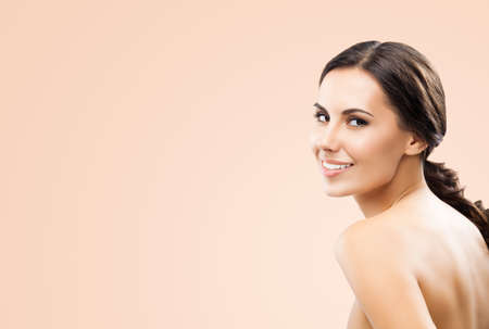 Portrait image of beautiful young happy smiling brunette woman, with naked shoulders, isolated over beige background. Copy space area.の写真素材