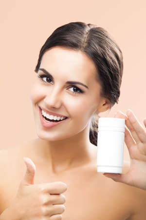 Beautiful happy smiling excited woman holding medical drug bottle of pills with mock up for advertising text place beige background. Cheerful girl show thumb up, healthcare and medicine ad conceptの写真素材