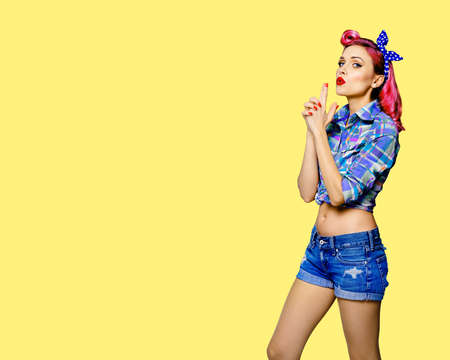 Pin up girl. Portrait of red purple attractive woman showing hand sign gesture. Retro and vintage concept. Yellow background with copy space text area. Pinup female model pose at studio.の写真素材