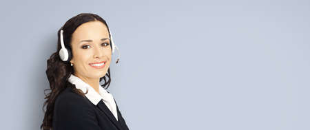 Call center help line service. Portrait photo of customer support phone sales agent operator in headset isolated on grey background. Happy smiling confident business woman. Caller worker. Receptionistの写真素材