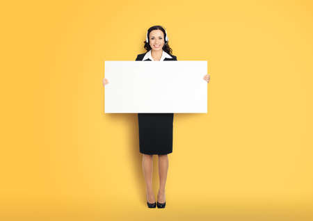 Call Center Service. Customer support or sales agent. Businesswoman or caller phone operator holding white banner. Full body of business woman in headset with empty signboard. Yellow color background.の写真素材