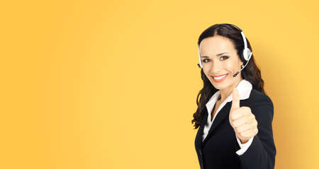 Call center service. Customer support phone sales operator in headset showing thumb up hand sign gesture, yellow color background with copy space area for text or ad slogan.の写真素材