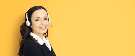 Call center help line service. Portrait photo of customer support phone sales agent operator in headset on yellow color background. Happy smiling confident business woman. Caller worker. Receptionistの写真素材