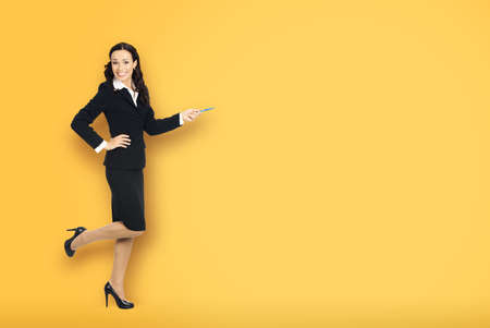 Full body length size view of happy excited smiling businesswoman showing pointing advertise at copy space. Confident business woman in black suit standing dancing over grey background.の写真素材