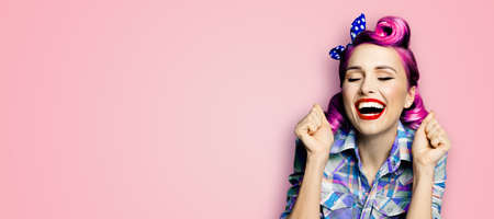 WOW! Unbelievable news! Excited surprised very happy purple red woman. Astonished pinup girl with open mouth and closed eyes, raised hands fists. Retro and vintage concept. Pink background. Wide imageの写真素材
