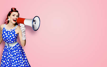 Portrait image of purple haired woman holding mega phone, shout advertising something. Girl in blue pin up style dress with mega phone loudspeaker. Isolated on rose pink background. Beauty model.の写真素材