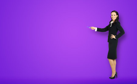 Full body length size view of happy excited smiling businesswoman showing pointing advertise at copy space. Confident business woman in black suit standing on violet purple background.の写真素材