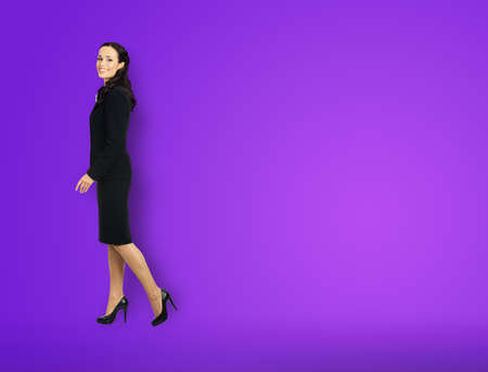 Full body length profile side photo of happy excited smiling businesswoman going side away, over copy space area. Waking confident business woman in black suit, violet purple backgroundの写真素材