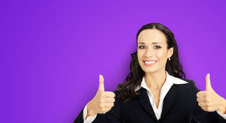 Businesswoman in black confident suit showing thumbs up gesture, violet purple background. Happy smiling gesturing brunette woman at studio. Business concept photoの写真素材