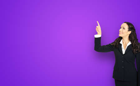 Profile portrait of smiling executive business woman in black confident suit, pointing showing up copy space. Violet purple background.の写真素材