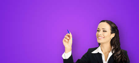 Portrait of happy smiling beautiful young businesswoman in black confident suit, writing or drawing something on screen, by marker. Brunette woman, violet purple backgroundの写真素材