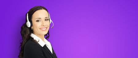 Call center help line service. Portrait photo of customer support phone sales agent operator in headset on violet purple background. Smiling confident business woman. Caller worker. Receptionistの写真素材